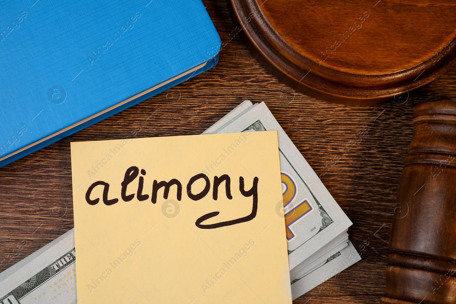 Photo of Card with word Alimony, dollar banknotes, gavel and notebook on wooden table, top view