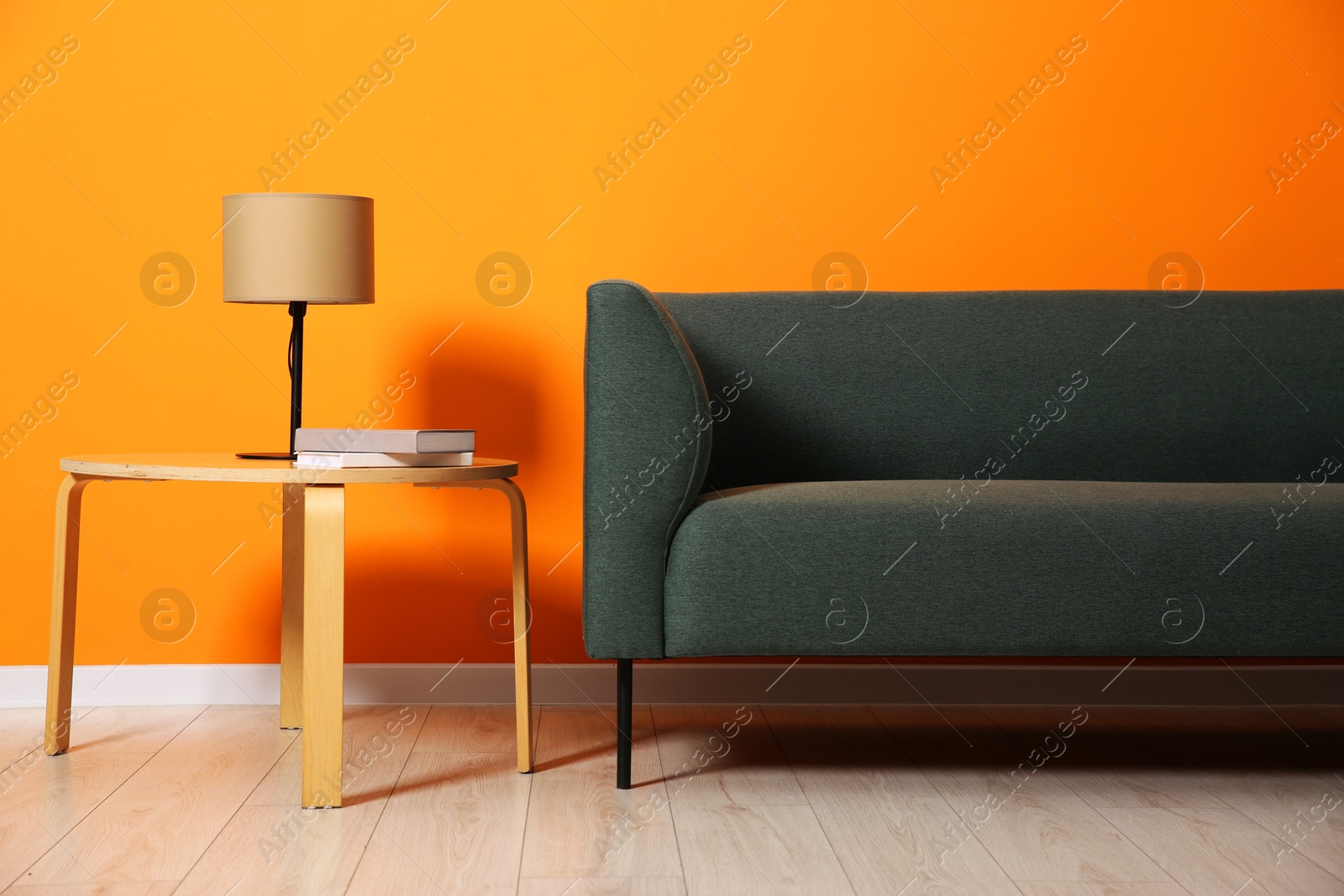 Photo of Stylish sofa, lamp and books on coffee table near orange wall