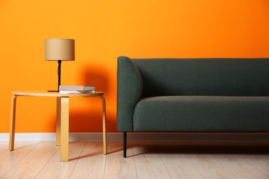 Photo of Stylish sofa, lamp and books on coffee table near orange wall