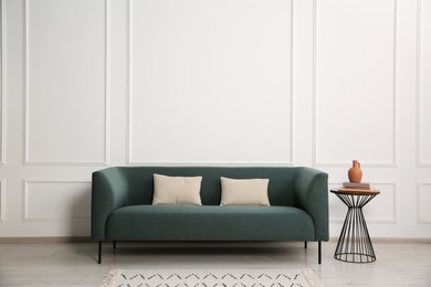 Photo of Stylish sofa with cushions and books on side table near white wall