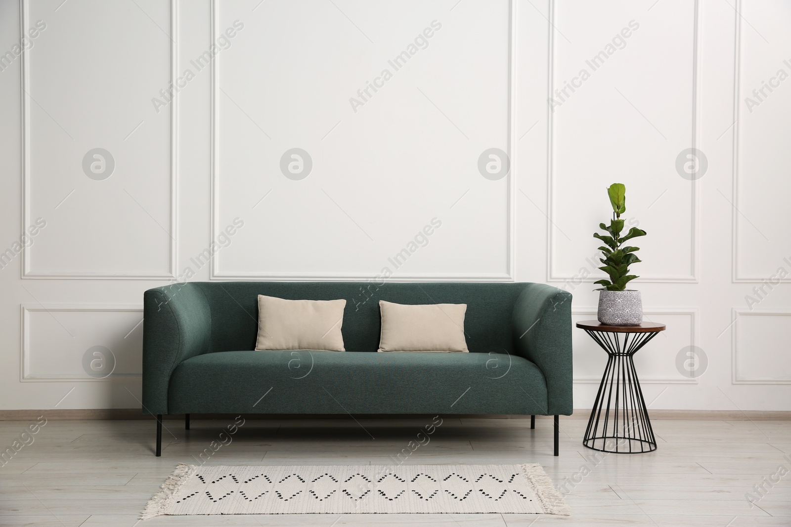 Photo of Stylish sofa with cushions and plant on side table near white wall