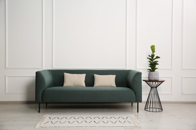 Photo of Stylish sofa with cushions and plant on side table near white wall