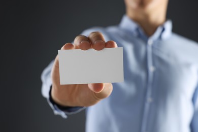 Man holding blank business card on grey background, closeup. Mockup for design