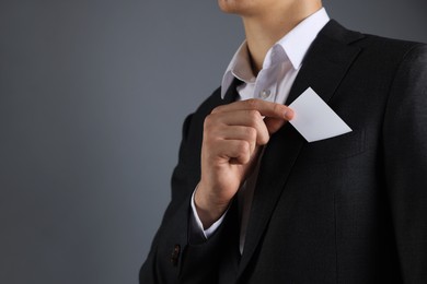 Photo of Man taking blank business card from pocket of his jacket on grey background, closeup. Mockup for design