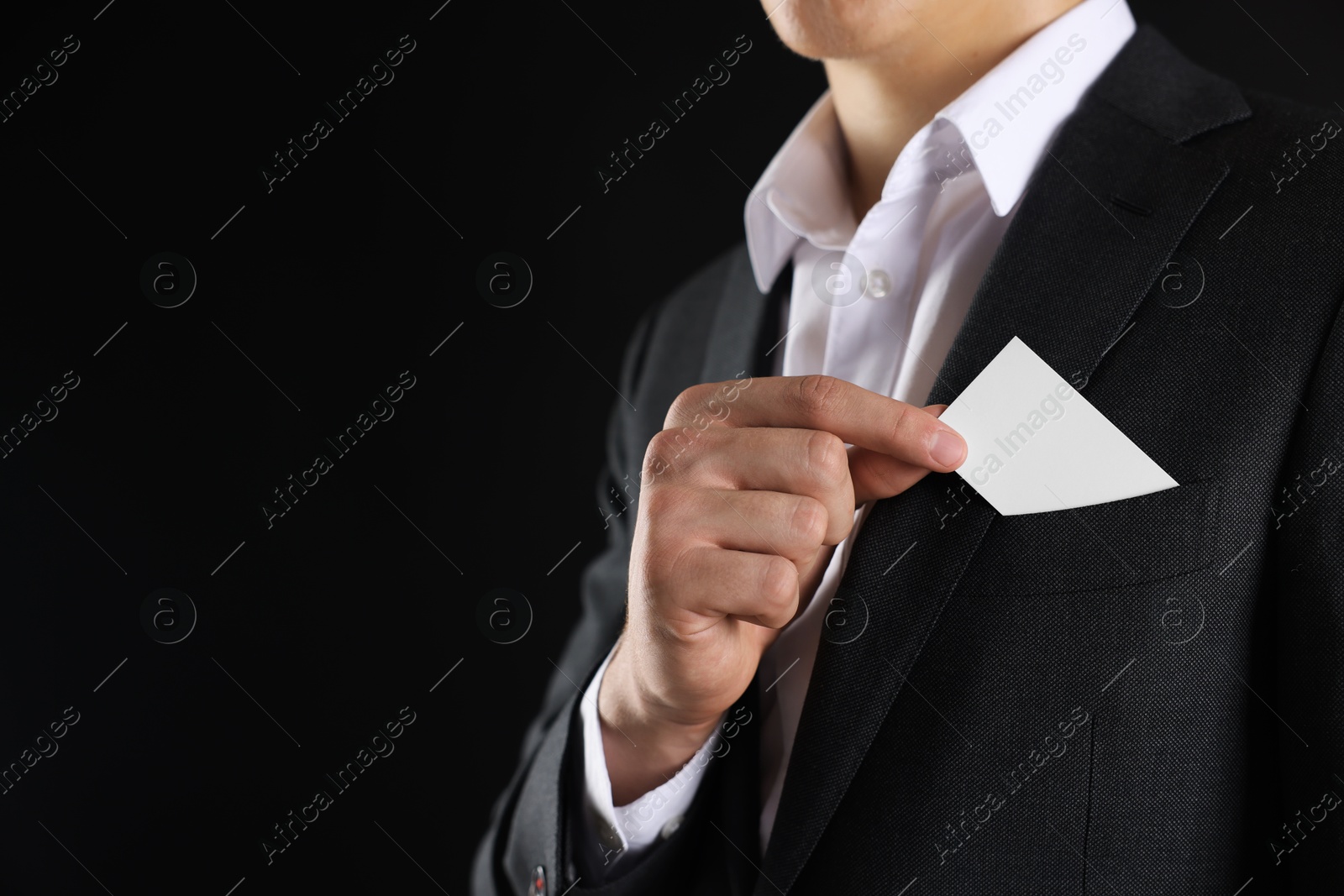 Photo of Man taking blank business card from pocket of his jacket on black background, closeup. Mockup for design