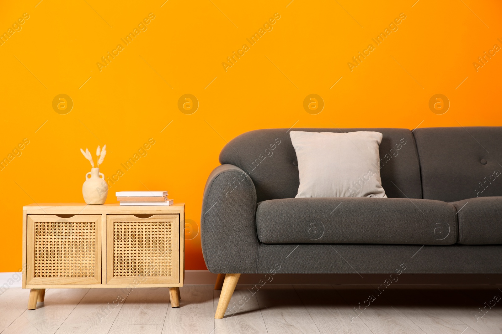 Photo of Stylish sofa, pillow and storage cabinet with decor near orange wall indoors