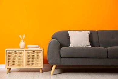 Photo of Stylish sofa, pillow and storage cabinet with decor near orange wall indoors