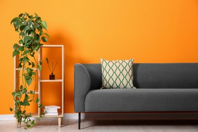 Photo of Stylish sofa, pillow and shelving unit with decor near orange wall indoors