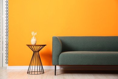 Photo of Stylish sofa and side table with decor near orange wall indoors