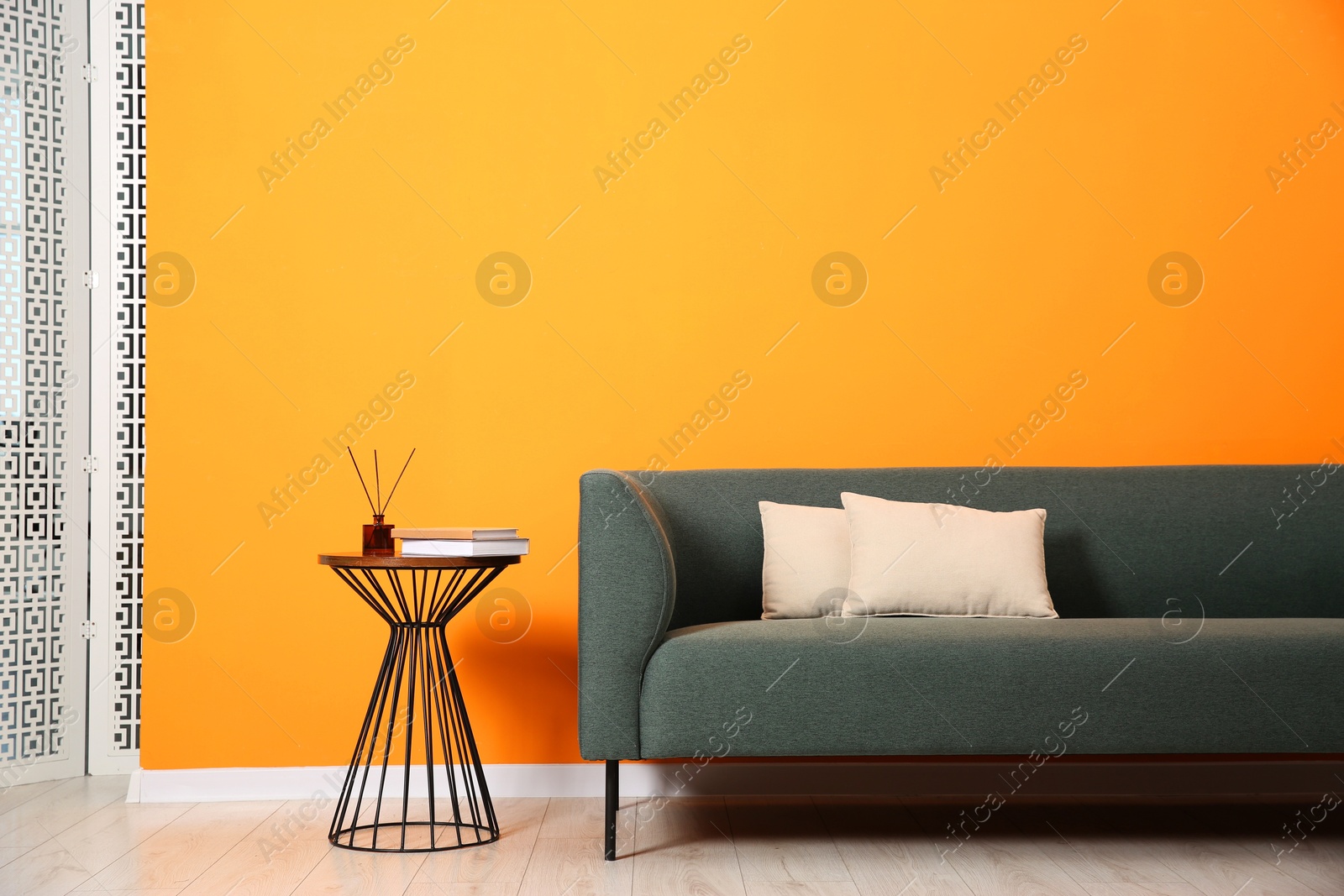 Photo of Stylish sofa, pillows and side table with decor near orange wall indoors