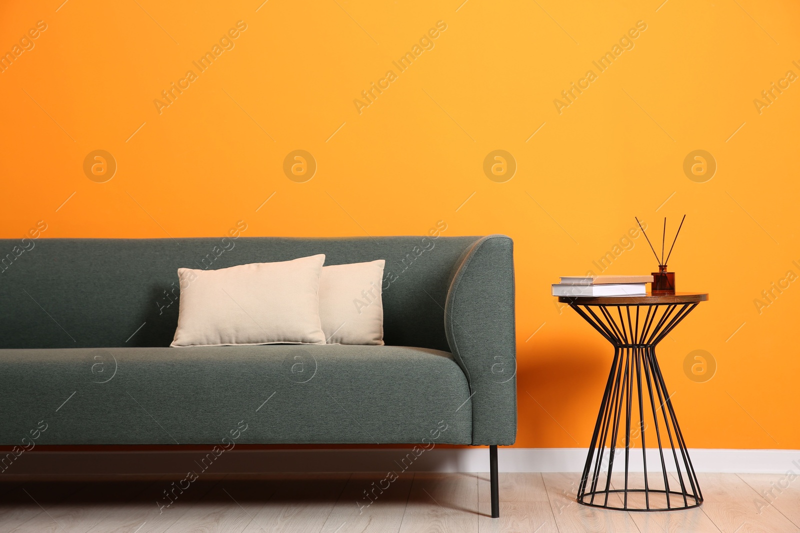 Photo of Stylish sofa, pillows and side table with decor near orange wall indoors