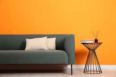 Stylish sofa, pillows and side table with decor near orange wall indoors