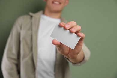 Man holding blank business card on green background, closeup. Mockup for design