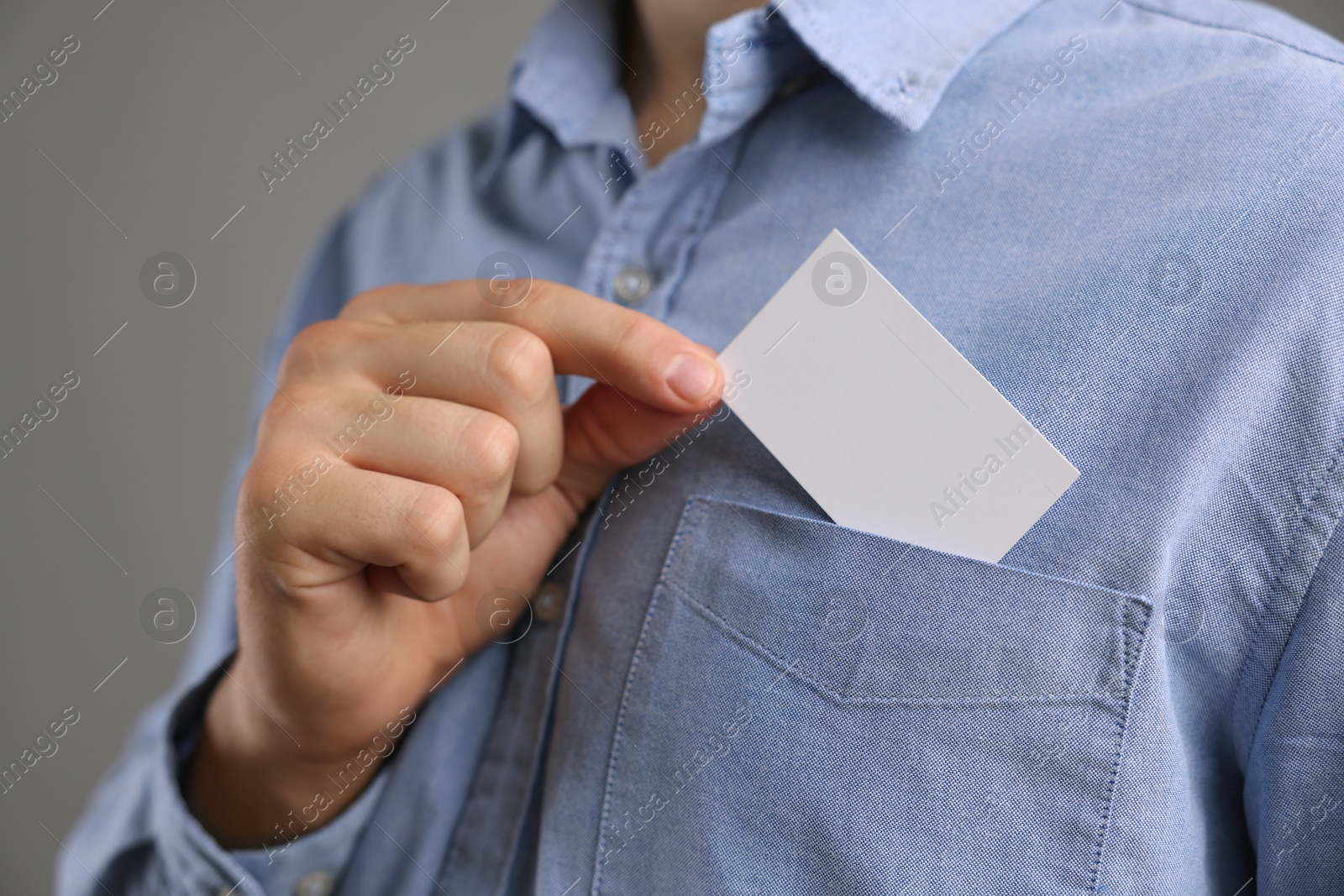 Photo of Man taking blank business card from pocket of his jacket on grey background, closeup. Mockup for design