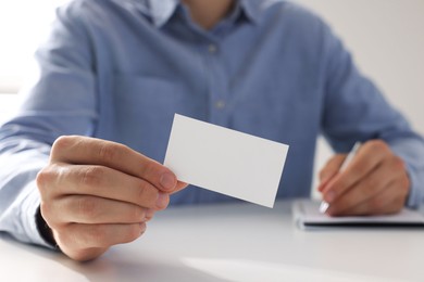 Man holding blank business card at table in office, closeup. Mockup for design