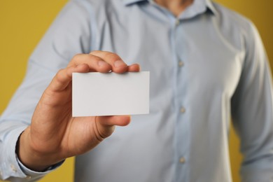 Man holding blank business card on yellow background, closeup. Mockup for design