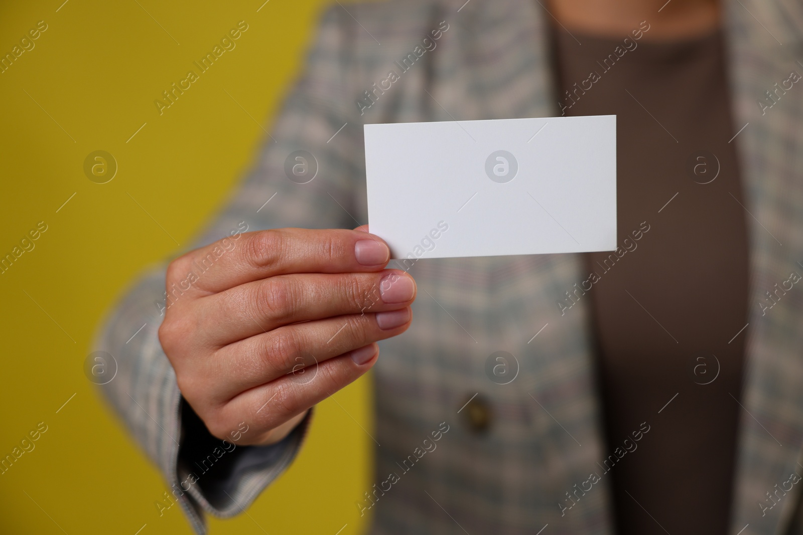 Photo of Woman holding blank business card on yellow background, closeup. Mockup for design