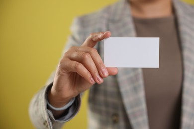 Woman holding blank business card on yellow background, closeup. Mockup for design