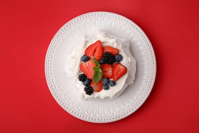 Photo of Pavlova cake (meringue dessert) with whipped cream, fresh berries and mint on red background, top view