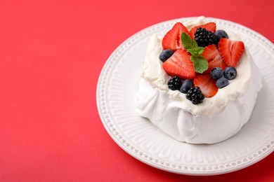 Photo of Pavlova cake (meringue dessert) with whipped cream, fresh berries and mint on red background, closeup. Space for text