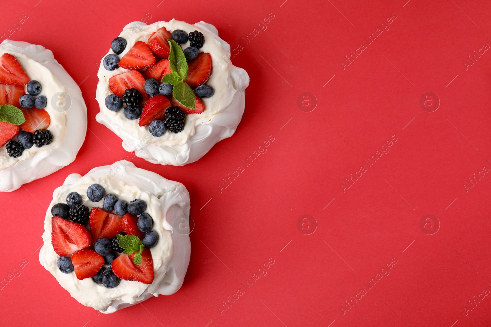 Photo of Pavlova cake (meringue dessert) with whipped cream, fresh berries and mint on red background, top view. Space for text