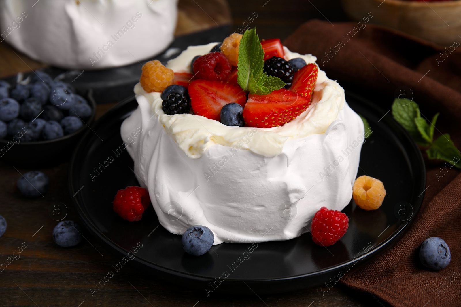 Photo of Pavlova cake (meringue dessert) with whipped cream, fresh berries and mint on wooden table, closeup