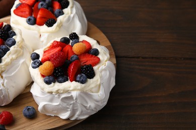 Photo of Pavlova cake (meringue dessert) with whipped cream and fresh berries on wooden table, closeup. Space for text