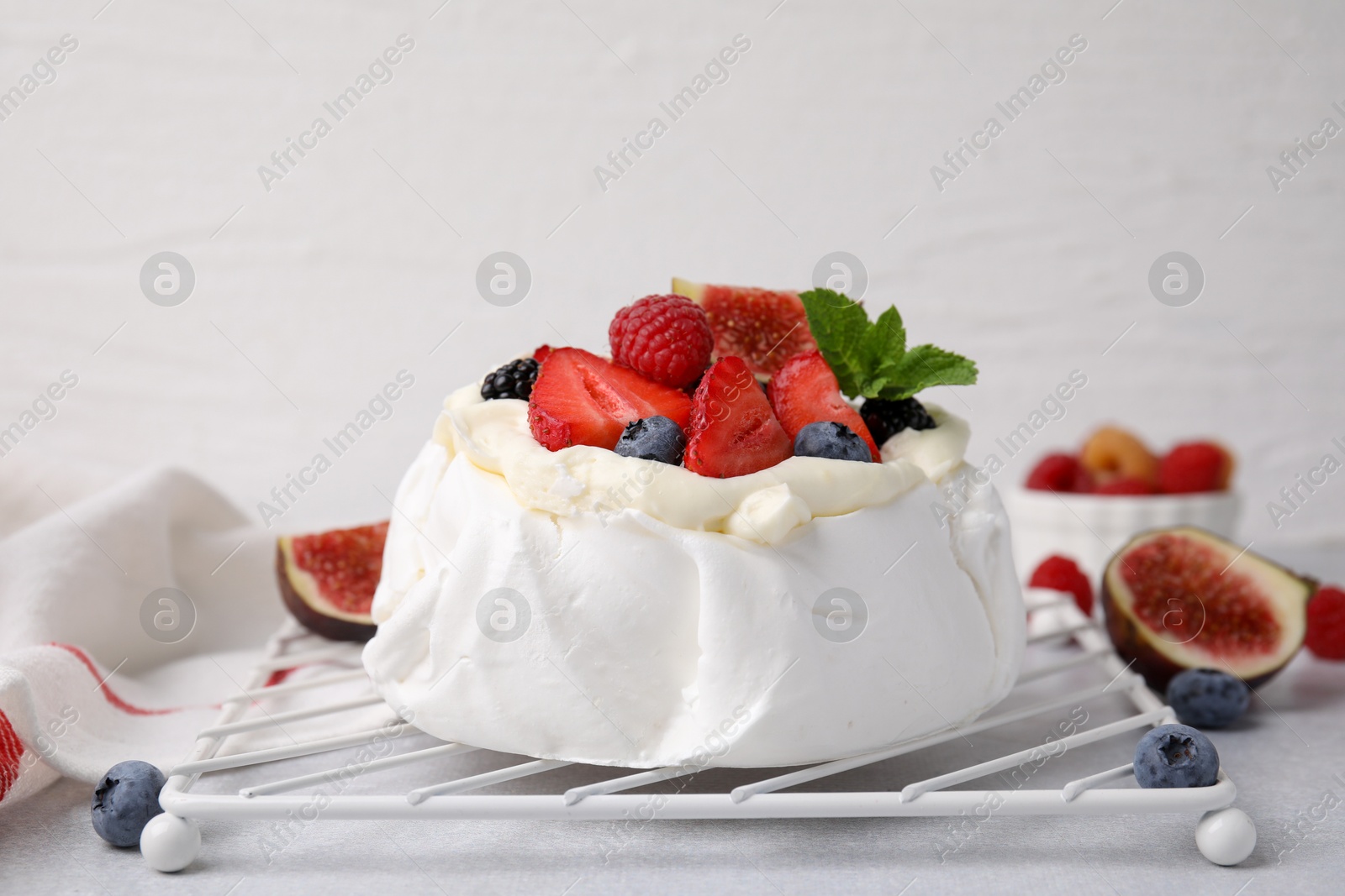 Photo of Pavlova cake (meringue dessert) with whipped cream, fresh berries, mint and fig on light grey table, closeup