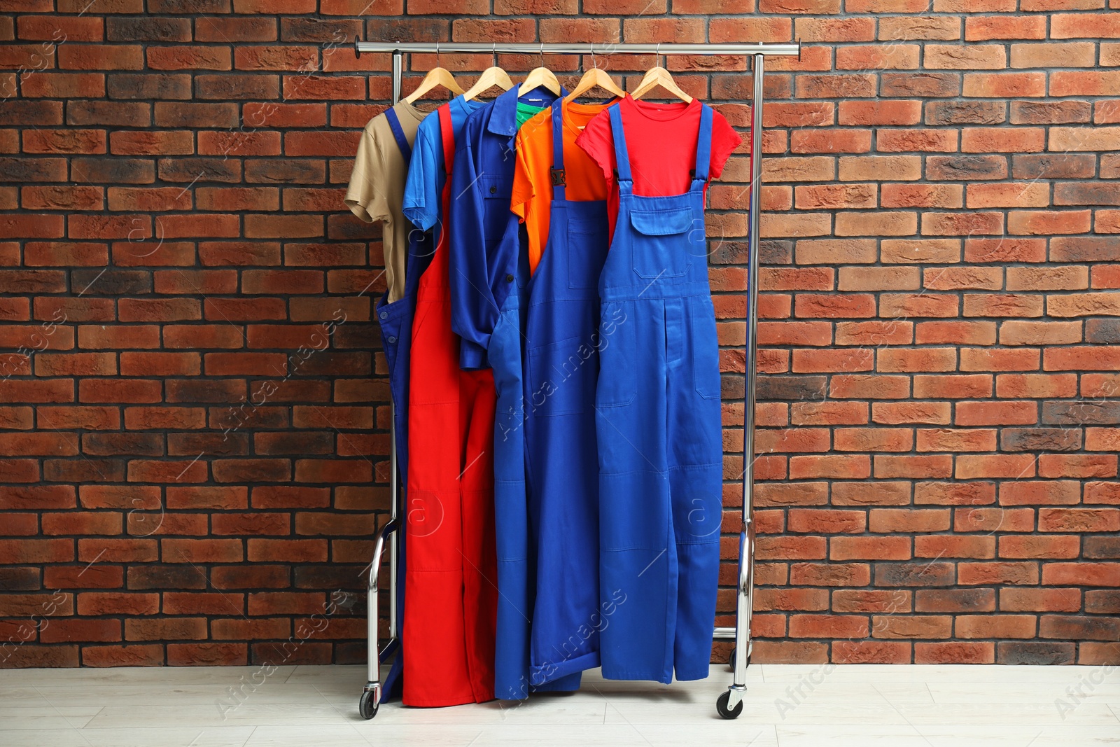 Photo of Different workers' uniforms on clothing rack near brick wall