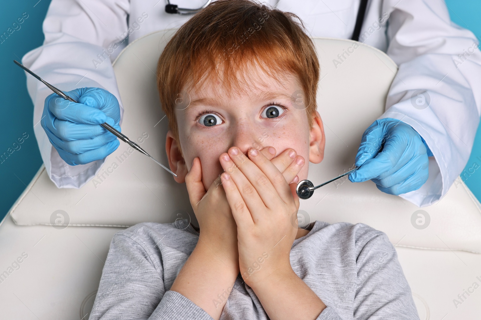 Photo of Dental phobia. Dentist working with scared little boy on light blue background