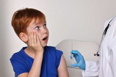 Dental phobia. Dentist with syringe near scared boy on light grey background