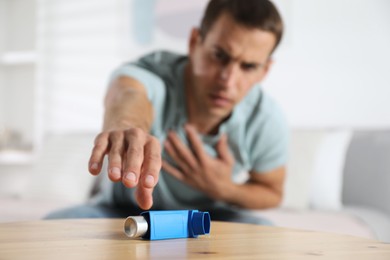 Man reaching for asthma inhaler at wooden table indoors, selective focus