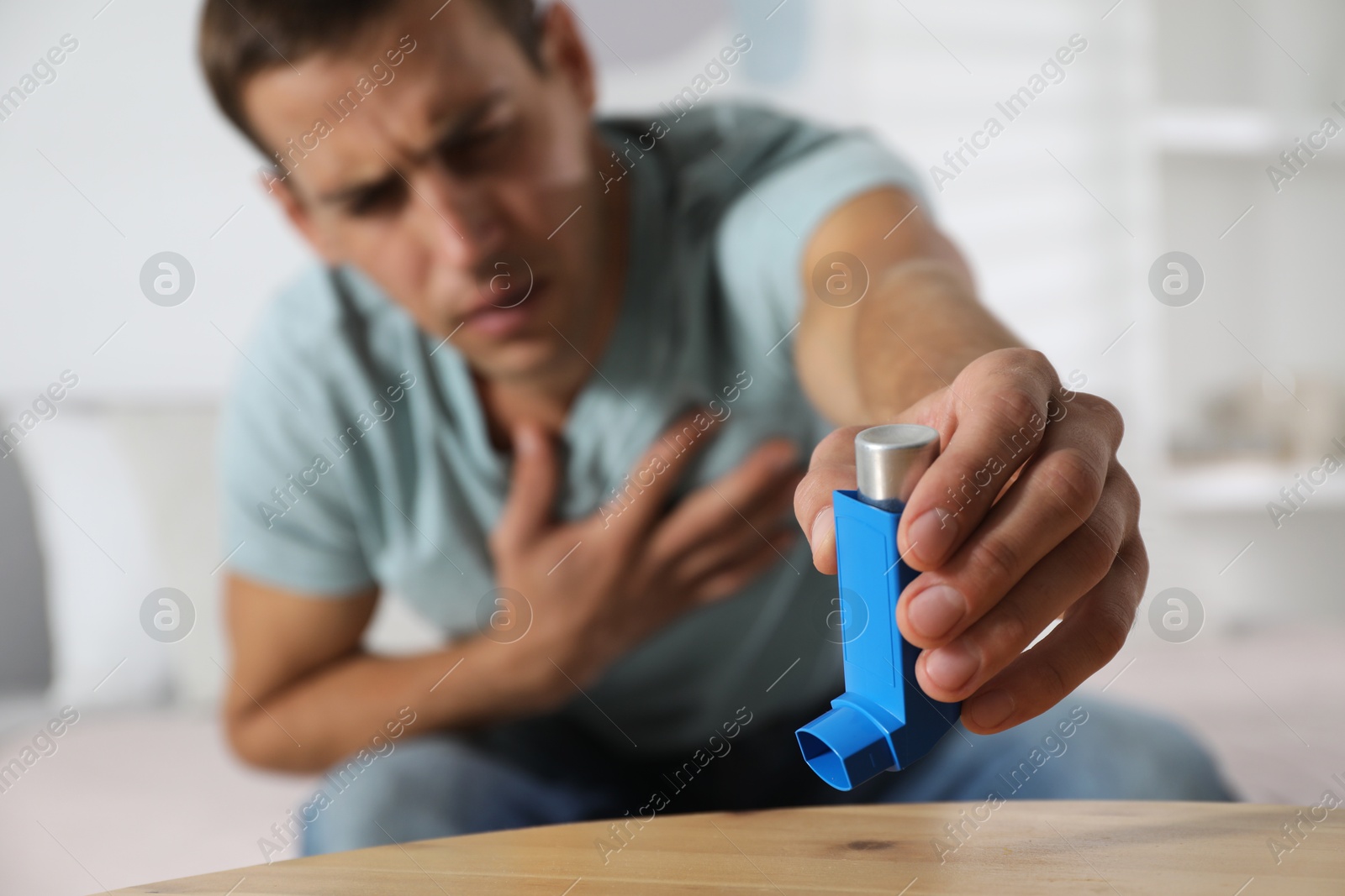 Photo of Man reaching for asthma inhaler at wooden table indoors, selective focus