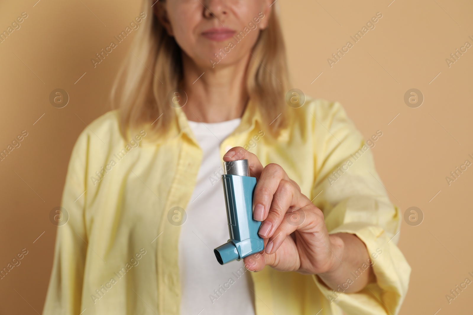 Photo of Woman holding asthma inhaler on beige background, closeup