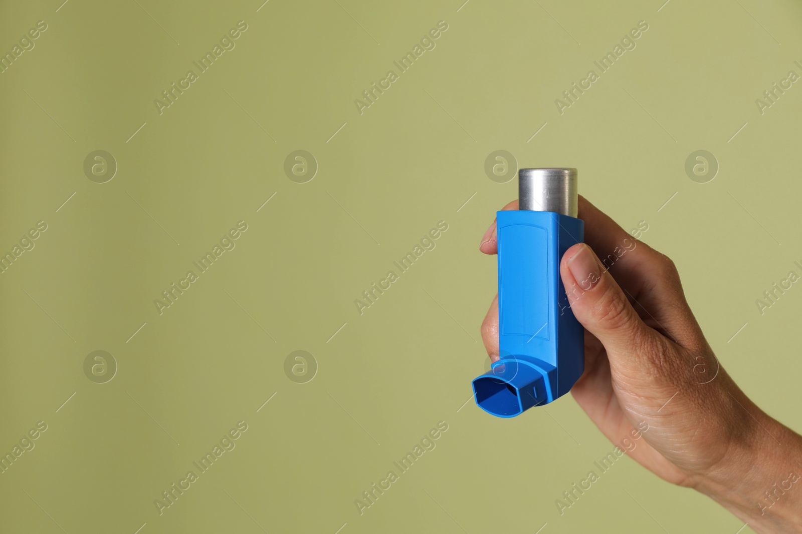 Photo of Woman holding asthma inhaler on olive background, closeup. Space for text