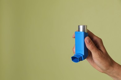 Woman holding asthma inhaler on olive background, closeup. Space for text