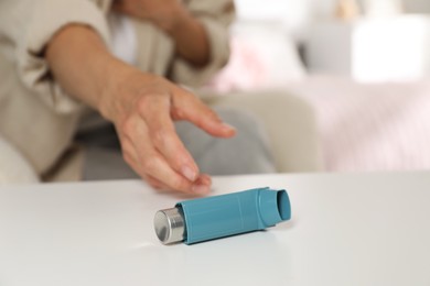 Woman reaching for asthma inhaler at white table indoors, closeup