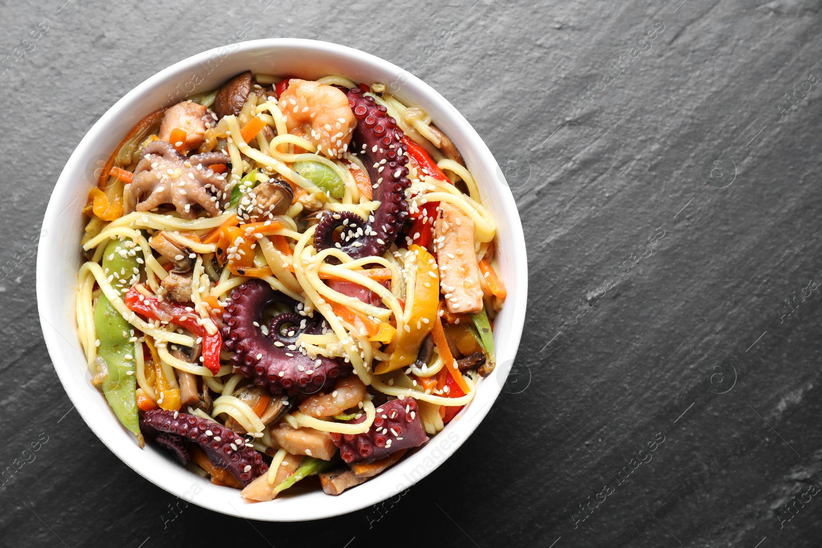 Photo of Stir-fry noodles with sea food in bowl on grey textured table, top view. Space for text