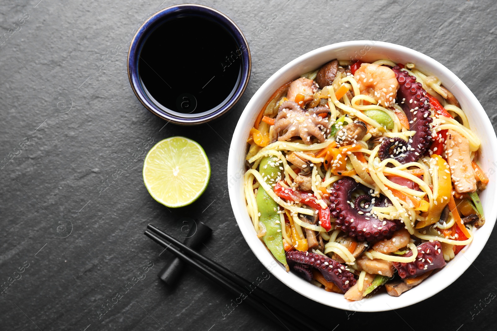 Photo of Stir-fry noodles with sea food served on grey textured table, flat lay