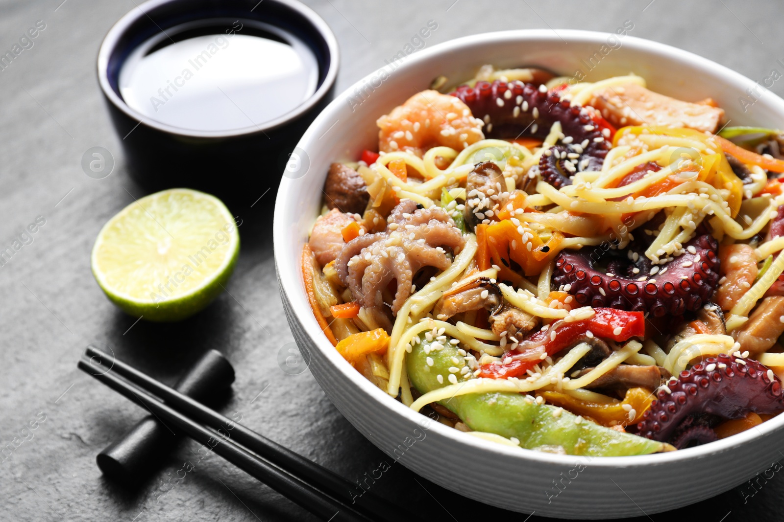 Photo of Stir-fry noodles with sea food served on grey textured table, closeup