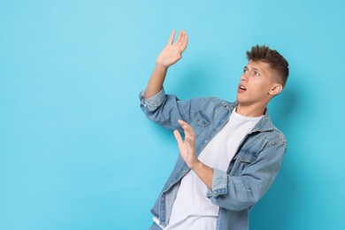 Portrait of scared young man on light blue background, space for text