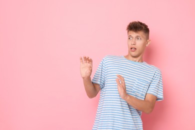 Portrait of scared young man on pink background, space for text