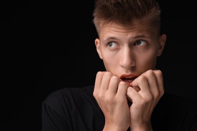 Portrait of scared young man on black background, space for text