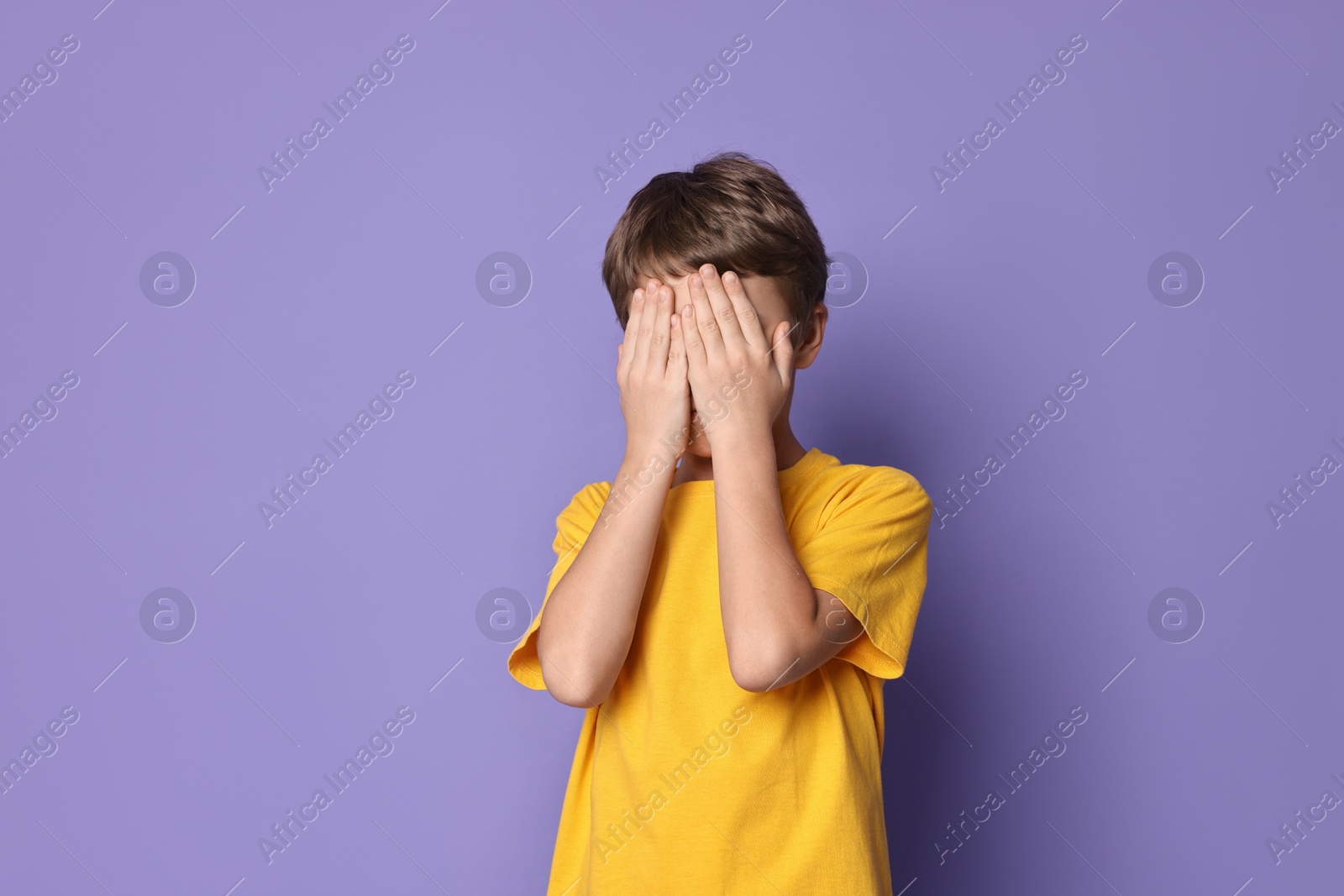 Photo of Scared little boy covering eyes on violet background. Space for text