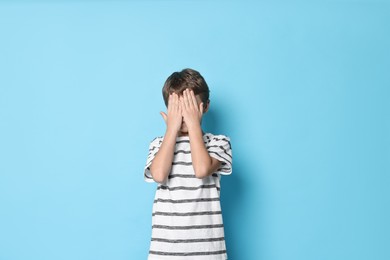 Scared little boy covering eyes on light blue background