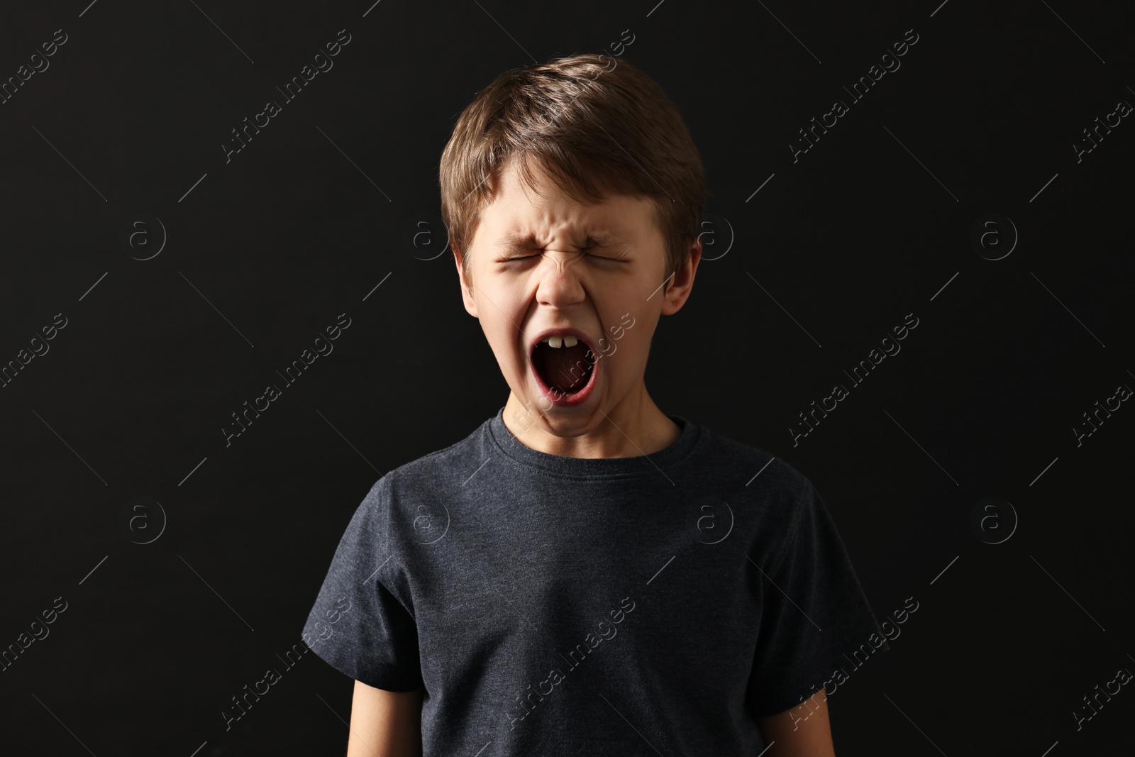 Photo of Scared little boy screaming on black background