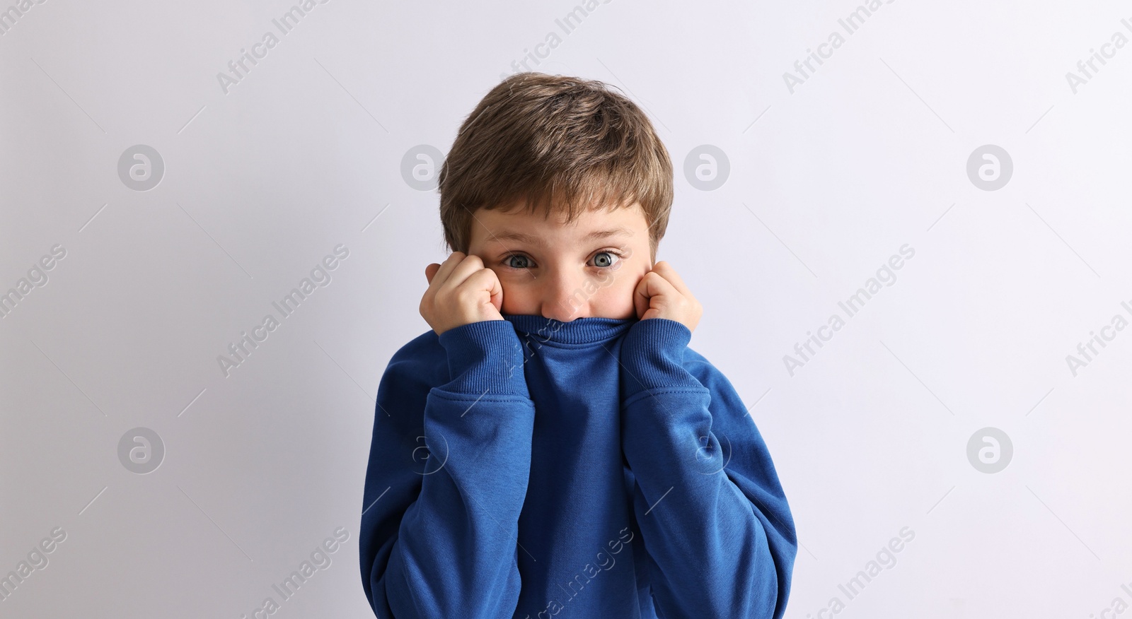 Photo of Scared little boy hiding on light background