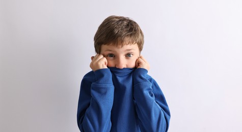 Scared little boy hiding on light background