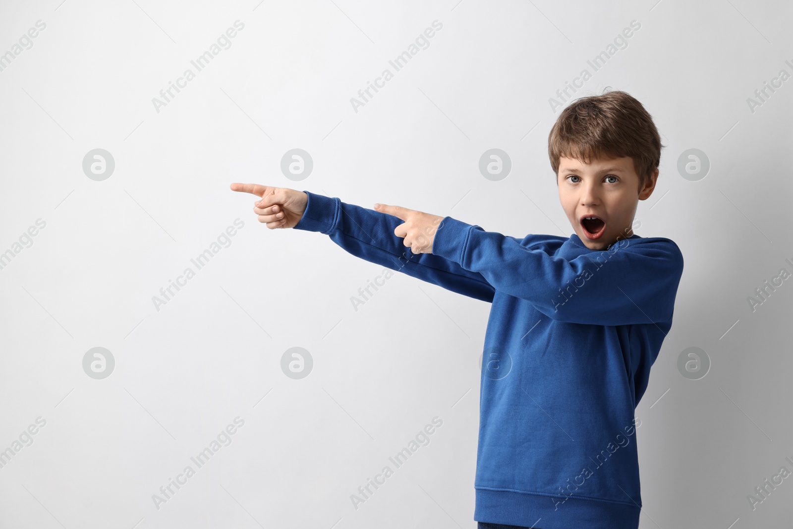 Photo of Scared little boy pointing at something on light background. Space for text