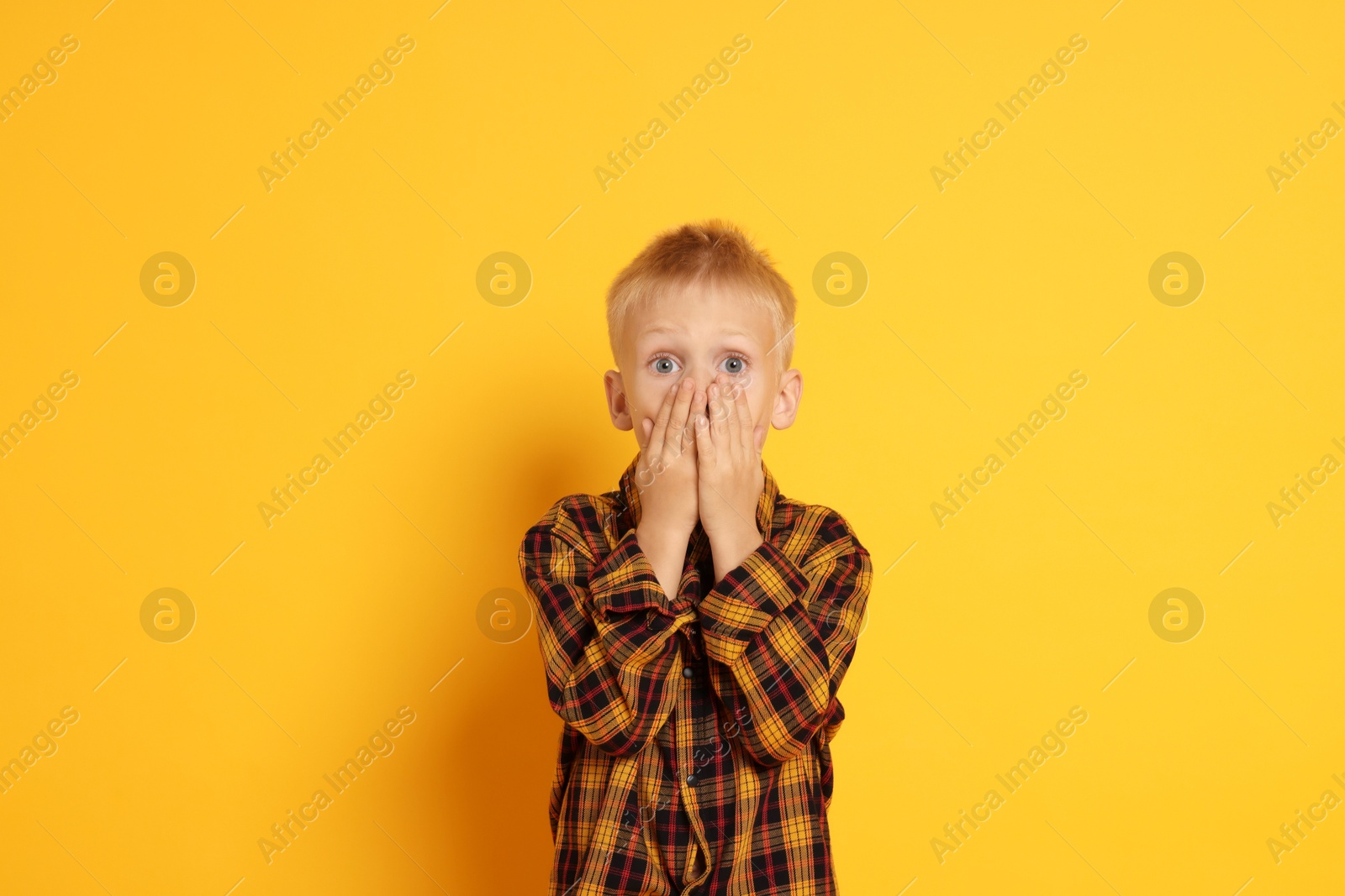 Photo of Scared little boy covering mouth on orange background